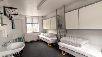Quarto em dormitório com pia, duas camas, janela e radiador.