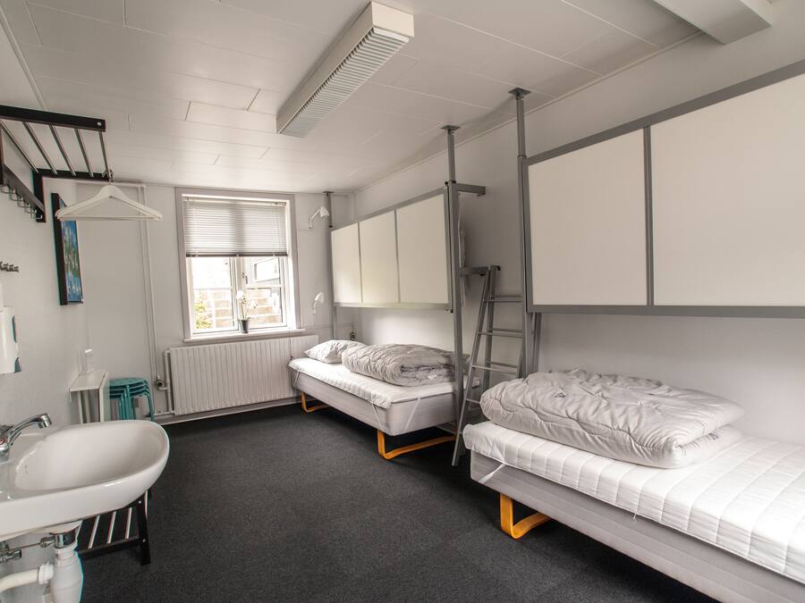 Quarto em dormitório com pia, duas camas, janela e radiador.