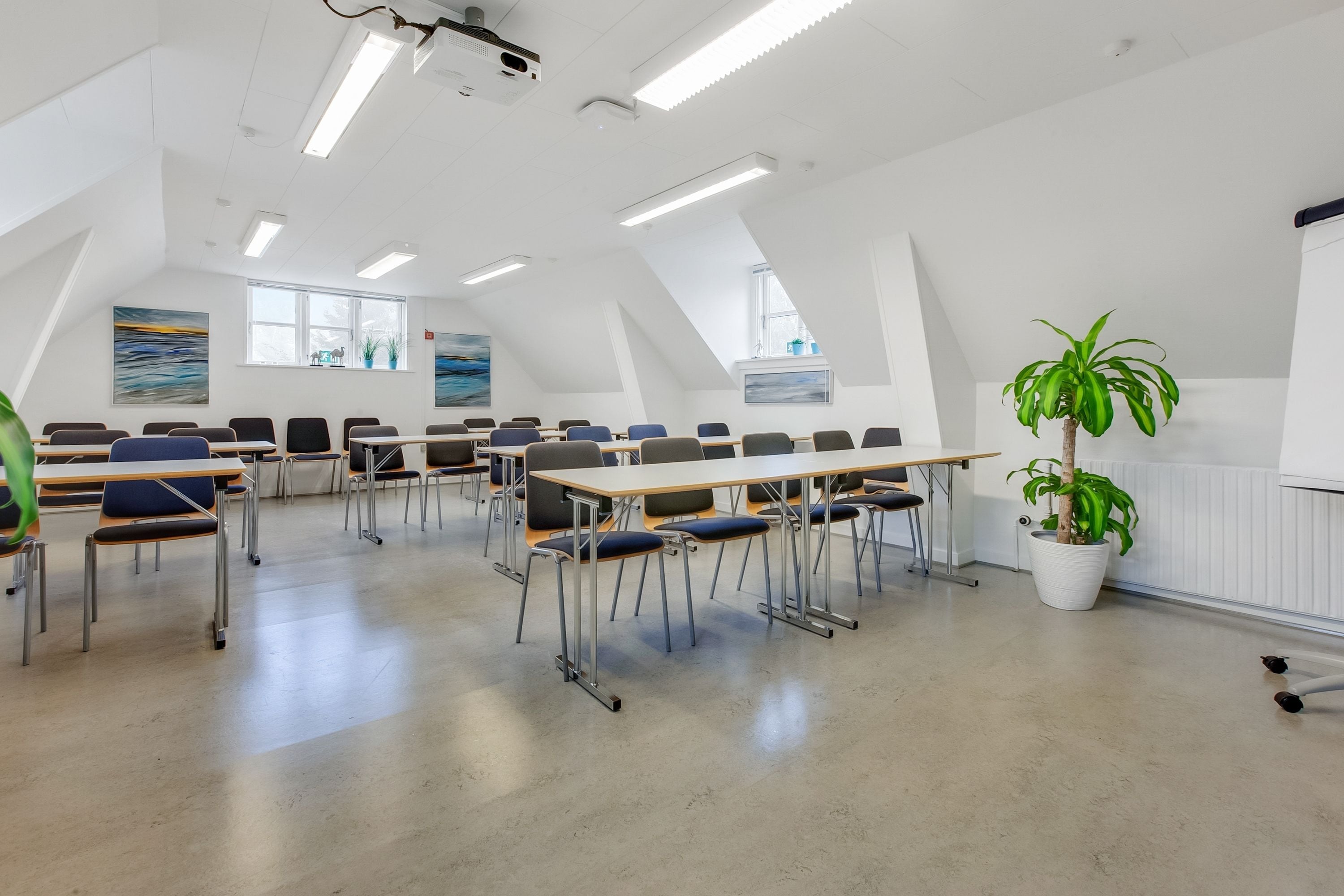 A classroom with desks and chairs arranged in rows, a projector, and a large window with a view.