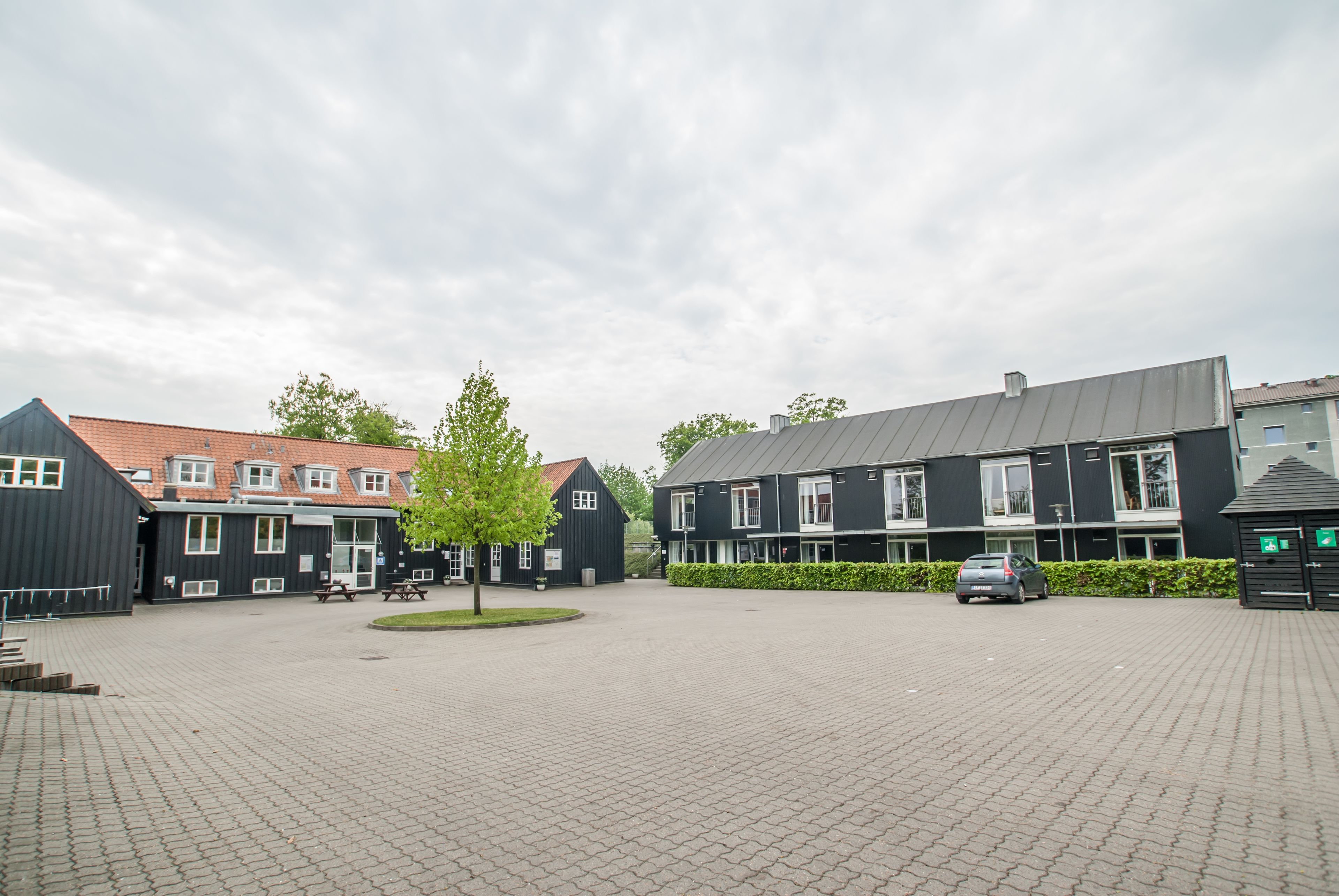 A courtyard with buildings, a car, and a tree.