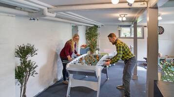 A room with a foosball table, a dartboard, and a foosball table in the background.