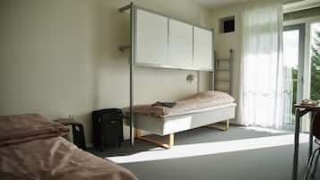 A bedroom with a bunk bed, a desk, a chair, a suitcase, and a window with curtains.