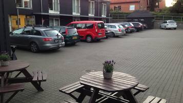 Un estacionamiento con varios coches, mesas de picnic y un edificio con ventanas.