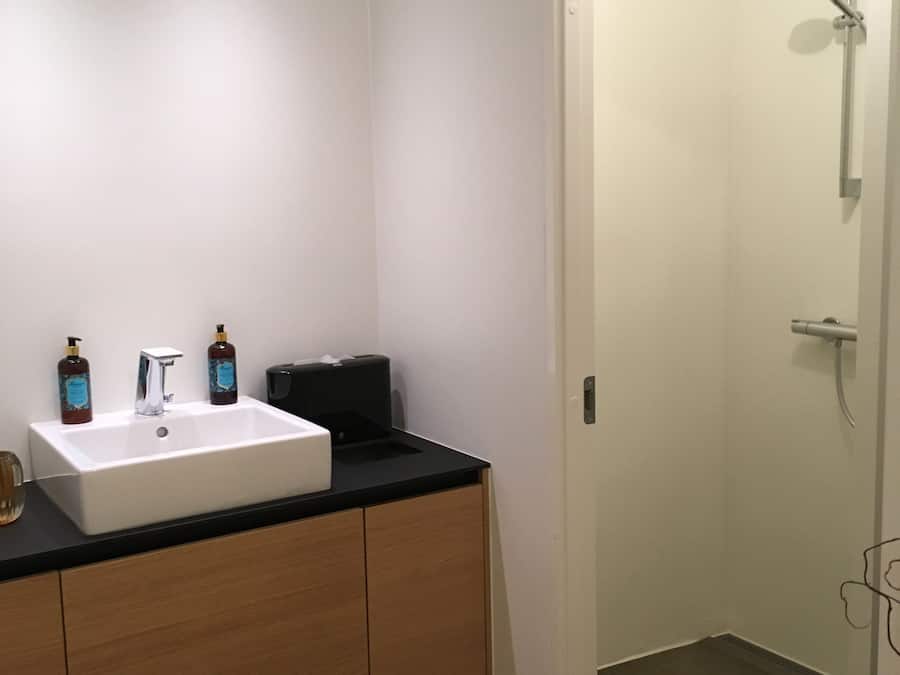 A modern bathroom with a white sink, wooden cabinets, and a shower area.