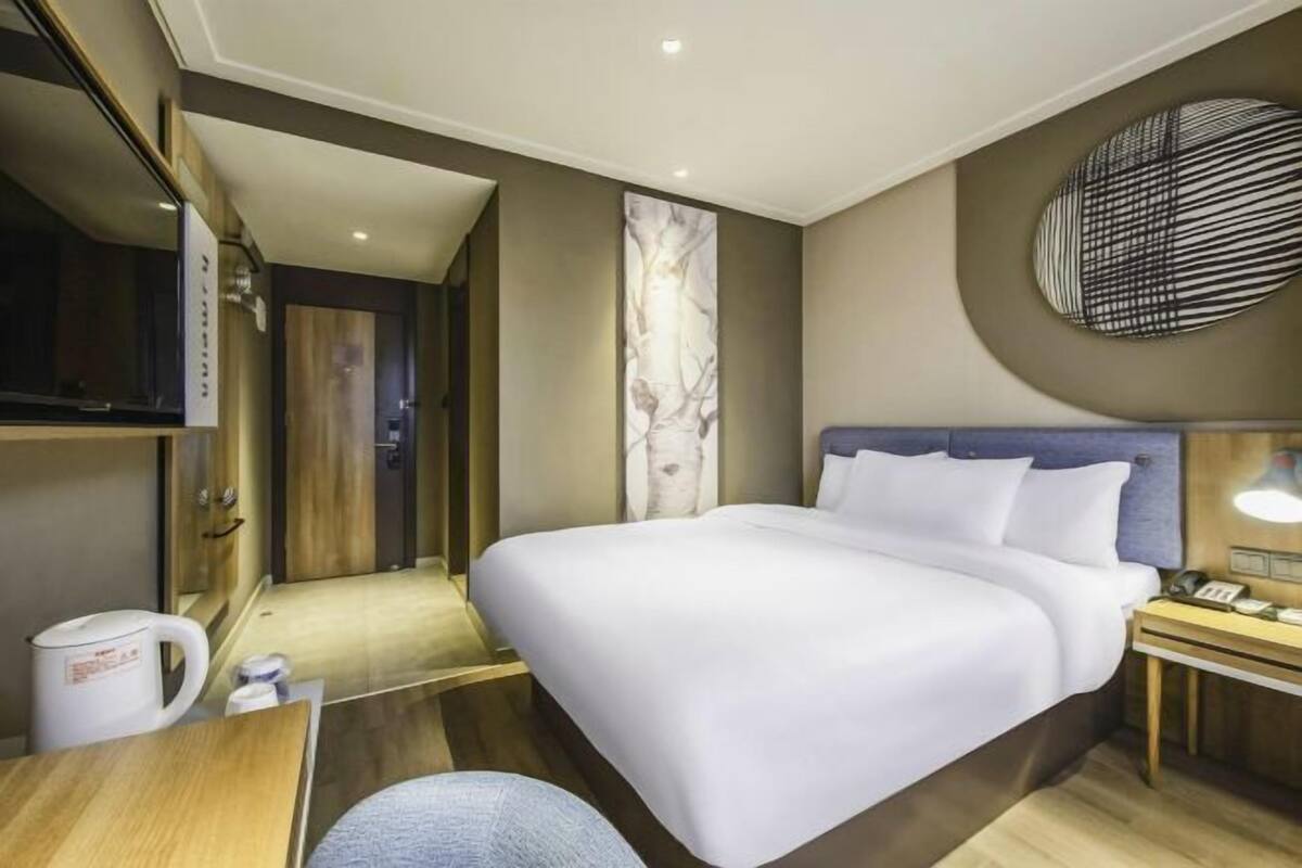 A hotel room with a bed, bedside table, lamp, and a wall-mounted artwork.
