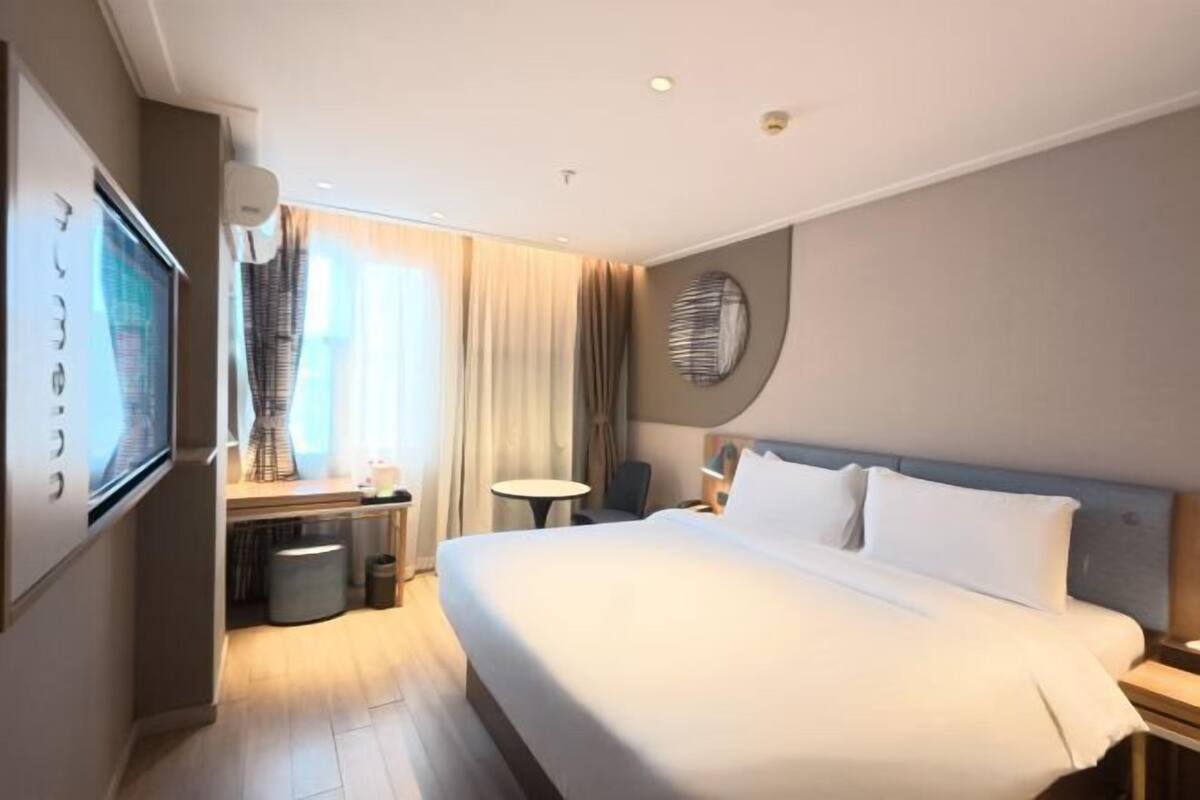 A hotel room with a large bed, a desk with a chair, a TV, and a round mirror on the wall.