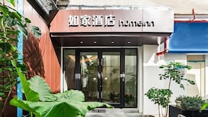 L’entrée d’un hôtel, avec une enseigne en langue étrangère, une porte en verre et des plantes en pot.