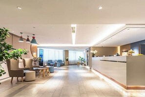 A hotel lobby with a reception desk, seating area, and a large plant.