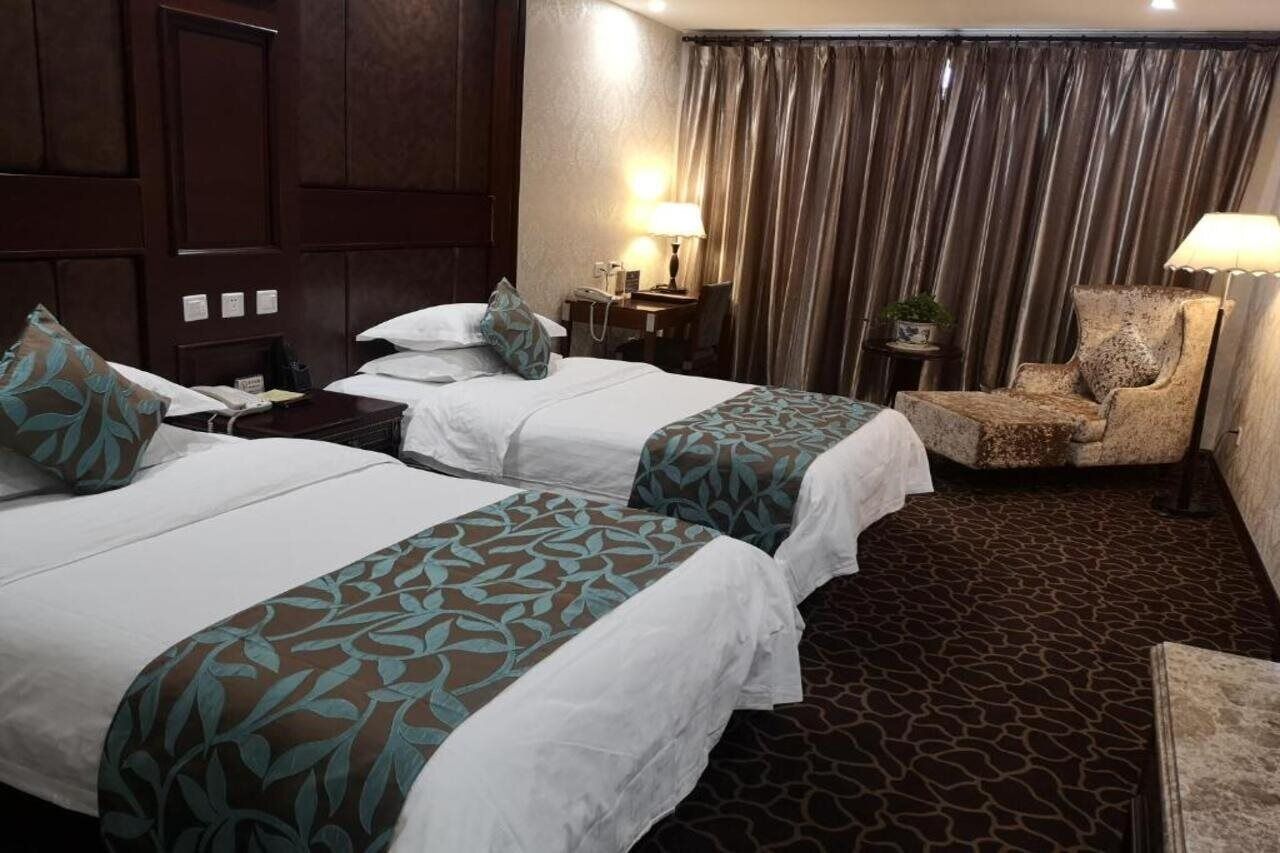 Habitación de hotel con dos camas, una silla, un escritorio y una lámpara.