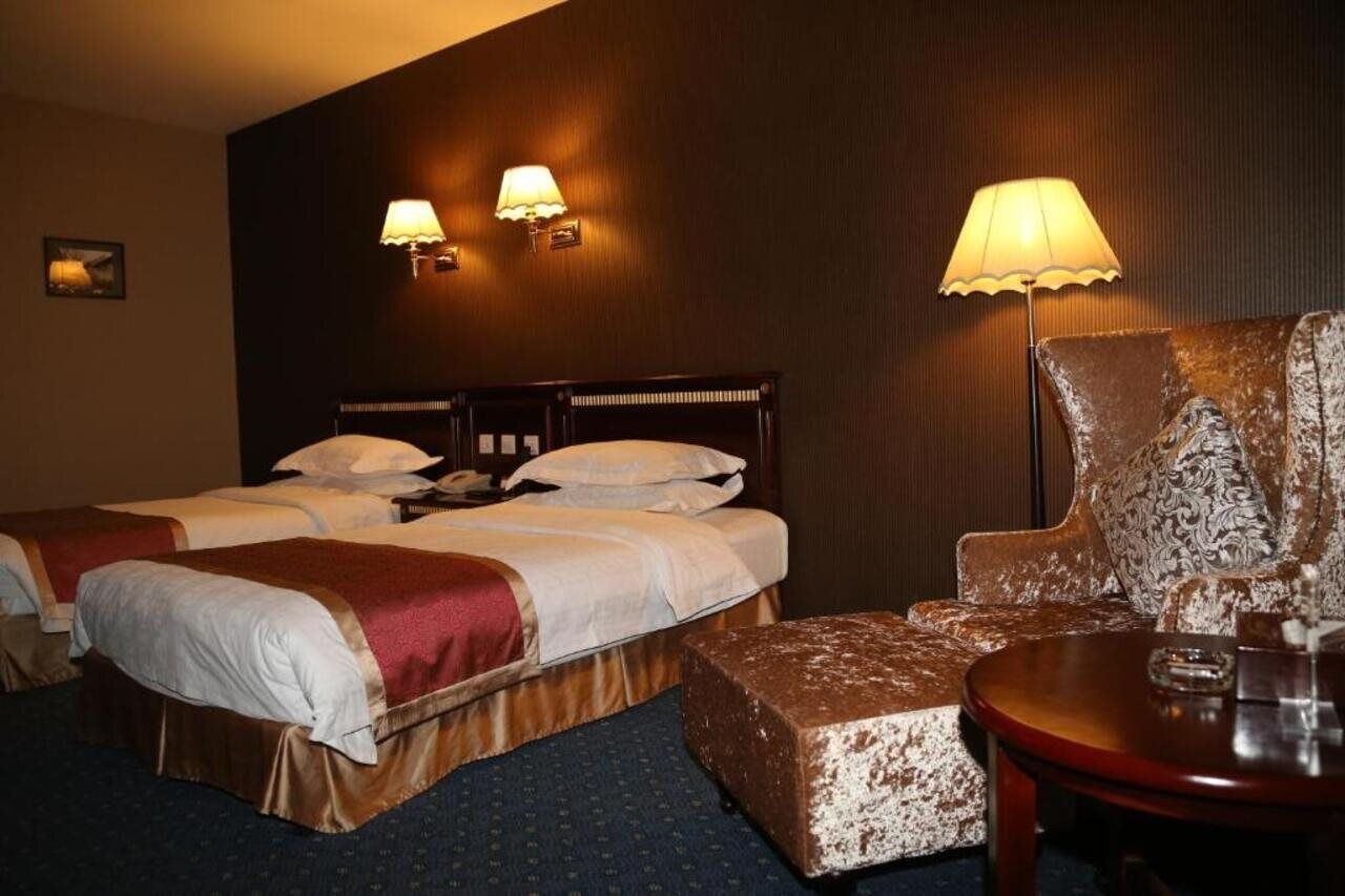 A hotel room with two beds, a sofa, a small table, and two wall-mounted lamps.