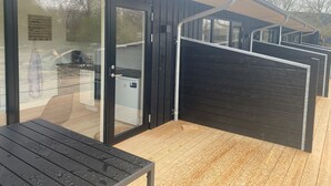 Een modern gebouw met een houten terras, een glazen entree en een metalen poort.