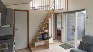 Een kleine keuken met een ingebouwde kookplaat, een houten trap met opbergplanken en een schuifdeur van glas die uitkomt op een balkon.