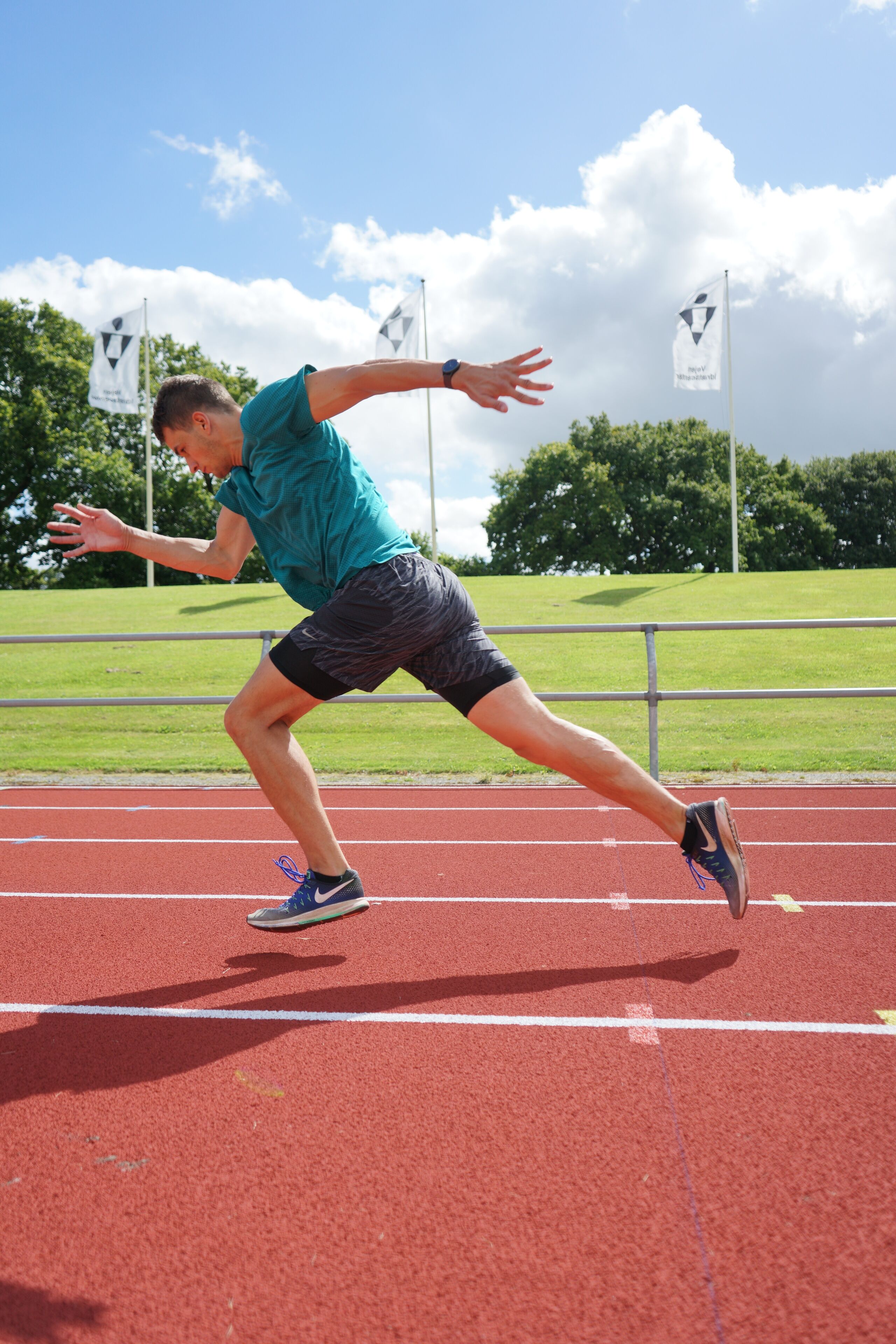 A person running on a red track with white lines, wearing a teal shirt and black shorts.