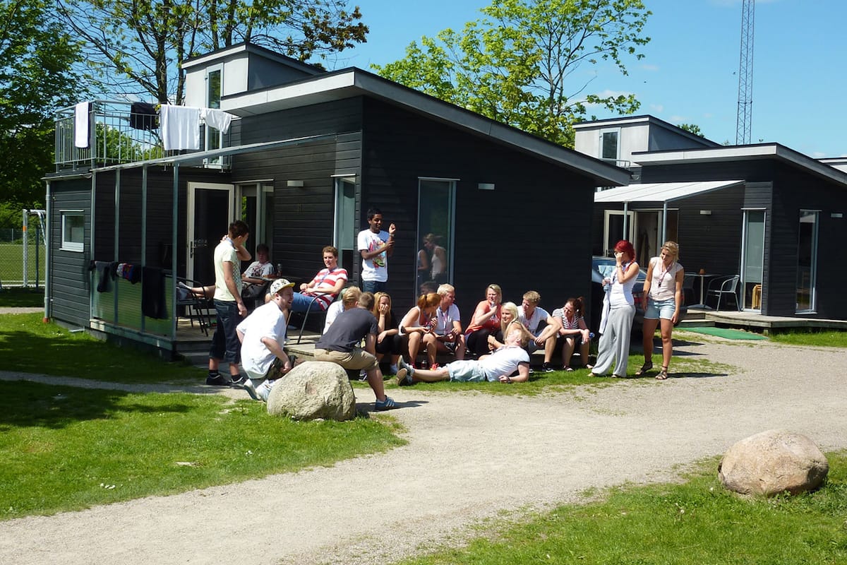 A group of people gathered around a modern building with large windows and a covered outdoor area.