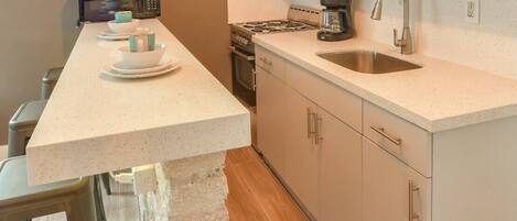 A kitchen with a long countertop, a sink, a stove, and cabinets.
