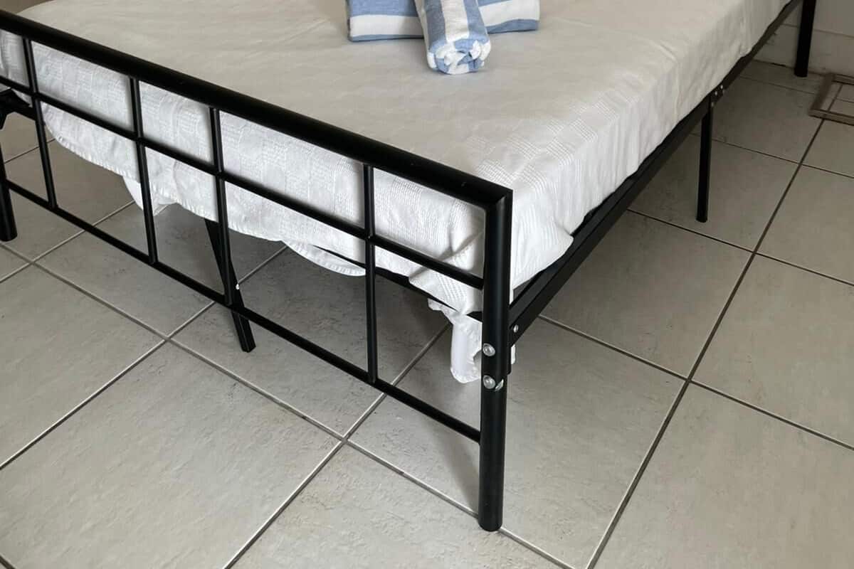 Un letto rifatto con lenzuola bianche e due asciugamani piegati, una lampada da comodino e una parete spoglia.