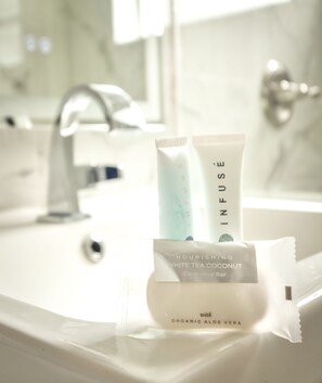 Une salle de bain avec un lavabo blanc, un miroir et un savon nettoyant à la noix de coco et au thé blanc nourrissant.