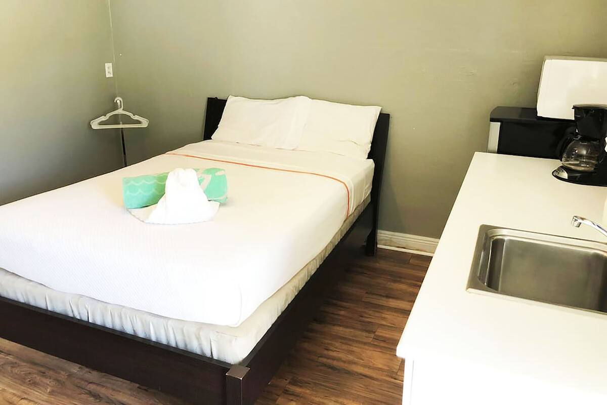 Una camera d'albergo con un letto, un piccolo comodino con una macchina del caffè, un appendiabiti e un lavandino.