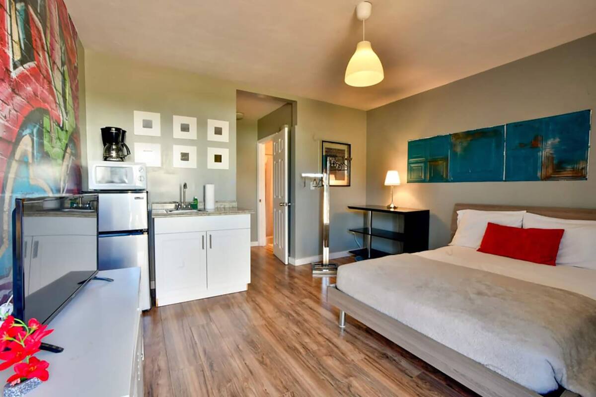 Una camera d'albergo moderna con un letto, una scrivania, un forno a microonde, una macchina del caffè e un quadro appeso al muro.