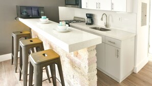 Eine moderne Küche mit Kochinsel, Barhocker, Mikrowelle, Kaffeemaschine und Spüle.