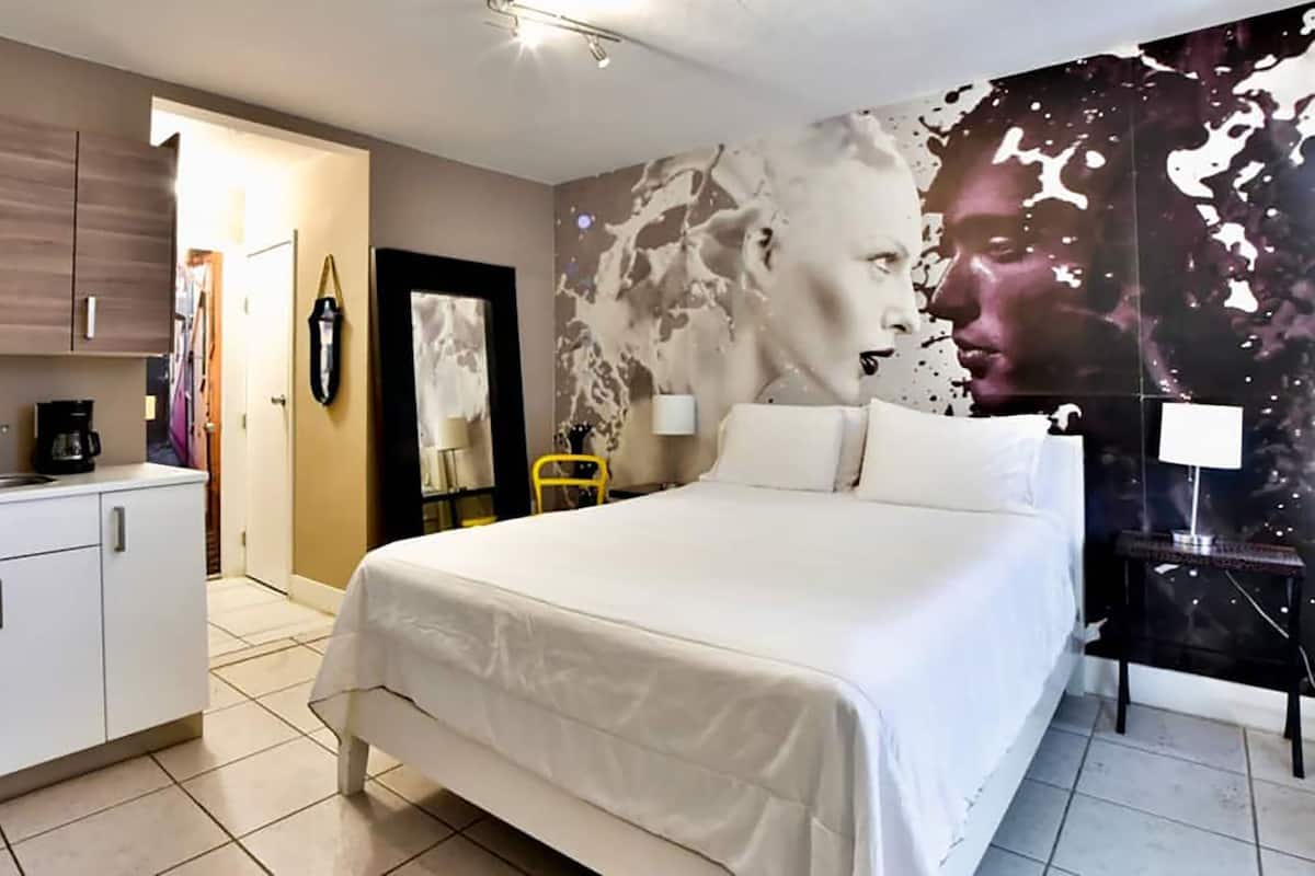 Una camera d'albergo con un letto, un armadio, una scrivania con una macchina per il caffè e una parete decorata da un grande dipinto astratto.