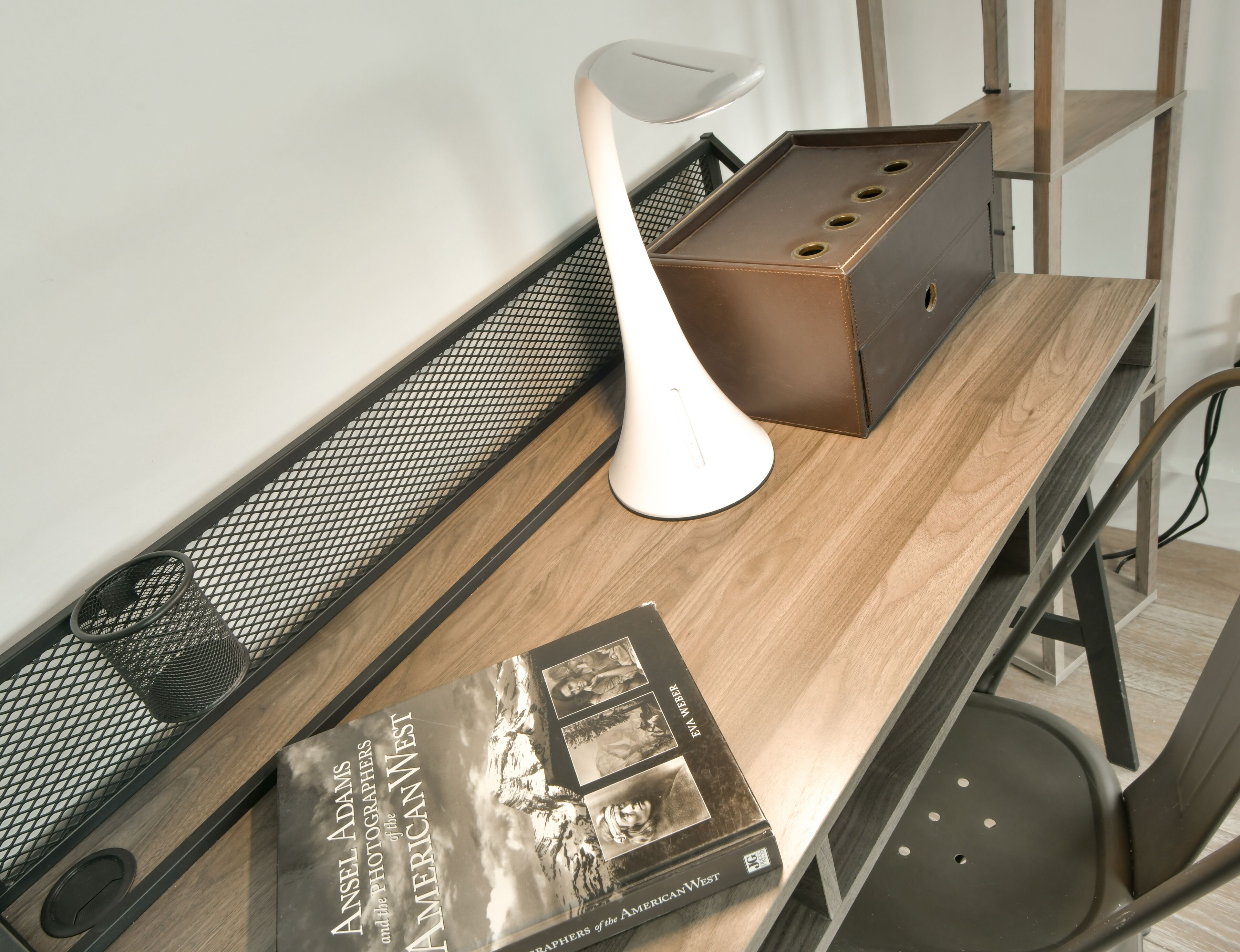 Un espace de travail moderne comprenant un bureau en bois, une chaise ergonomique blanche, une étagère en métal et un livre intitulé « Angels Adams et les photographes de l’Ouest américain ».