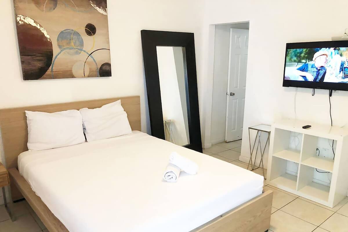 Camera d'albergo con un letto di legno, biancheria bianca, uno specchio grande, una TV su un mobile e una porta che conduce a un'altra stanza.