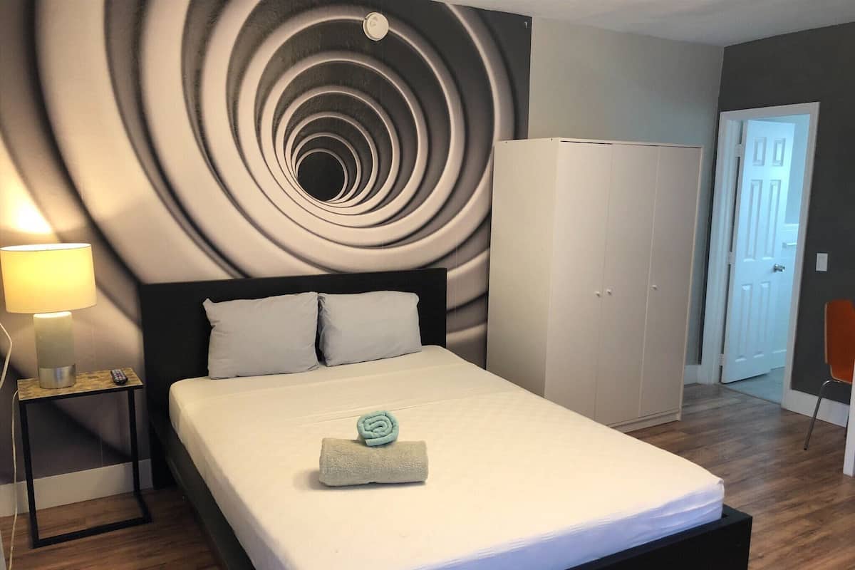 Una camera d'albergo moderna con un design a spirale, un letto con lenzuola bianche, un comodino con una lampada e un armadio.