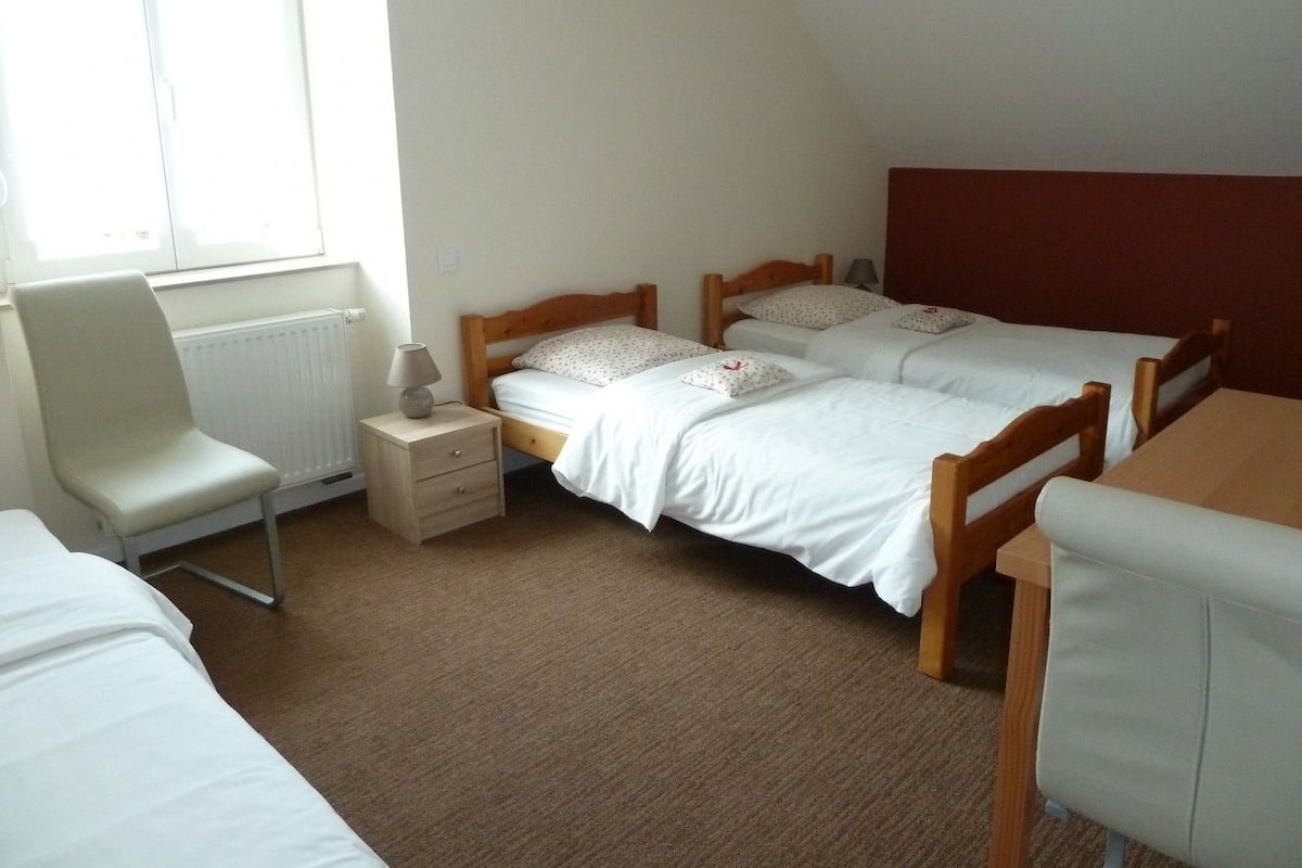 A room with two single beds, a chair, a small table, and a window with blinds.