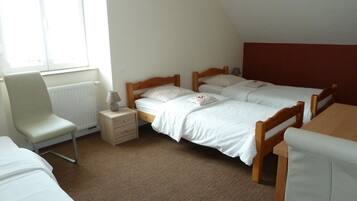 A room with two single beds, a chair, a small table, and a window with blinds.