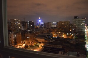Een stadsgezicht 's nachts met hoge gebouwen, een opvallende verlichte toren en een uitzicht door een raam.