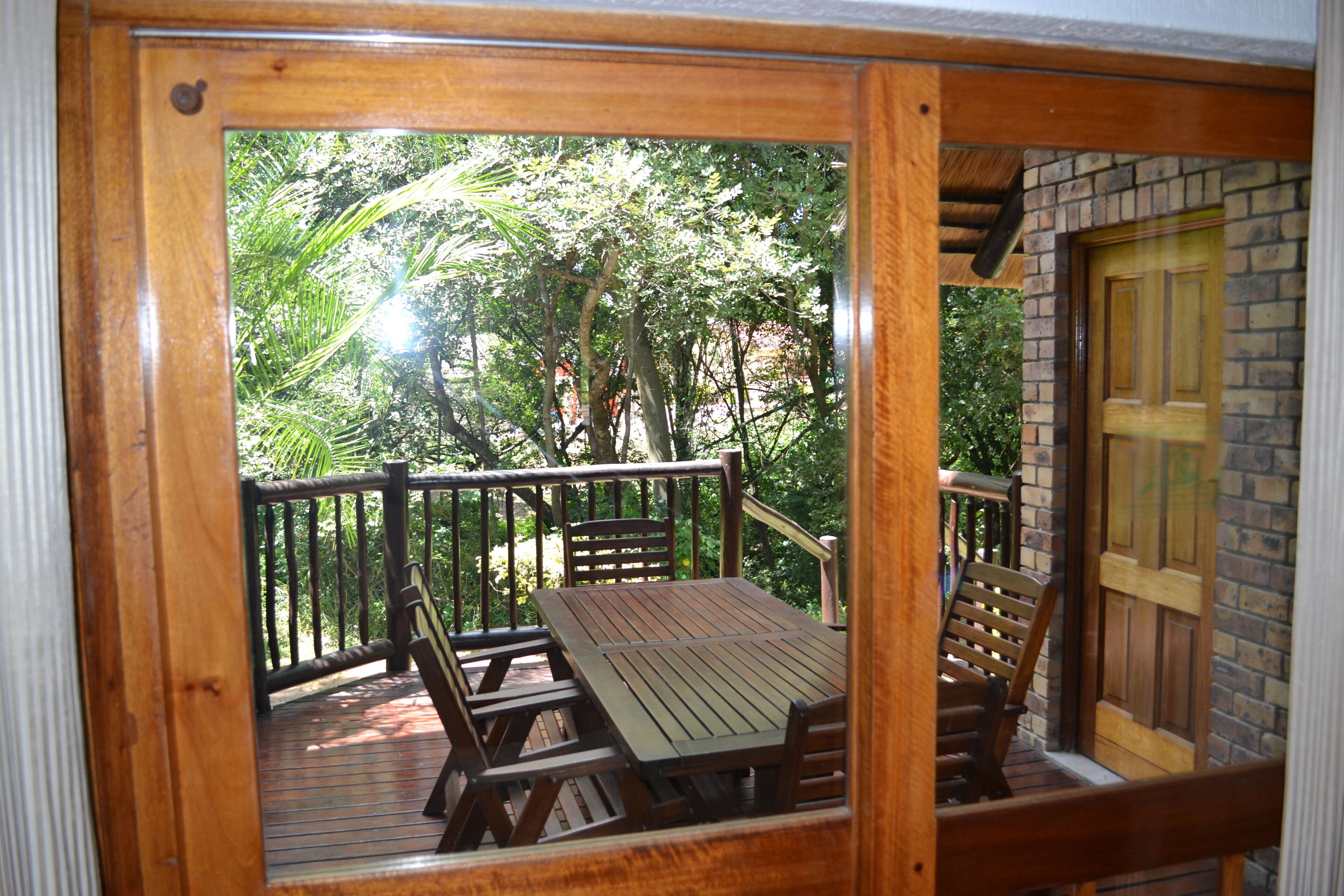Une terrasse en bois avec une table et des chaises, entourée d’un mur de briques et d’une porte en bois.