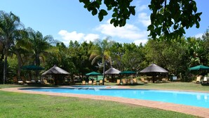 A swimming pool with lounge chairs and thatched-roof gazebos. - Kruger Park Lodge - Golf Safari SA (Mbombela)
