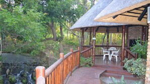 A wooden bridge leading to a thatched-roof pavilion with outdoor seating. - Kruger Park Lodge - Golf Safari SA (Mbombela)