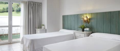 A hotel room with two beds, a sliding glass door to the outside, a small table with a plant, and a wall-mounted light fixture.
