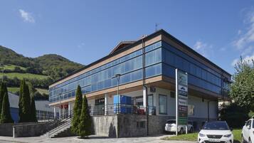 A modern building with a glass facade, a staircase leading to the entrance, and a parking area with cars.