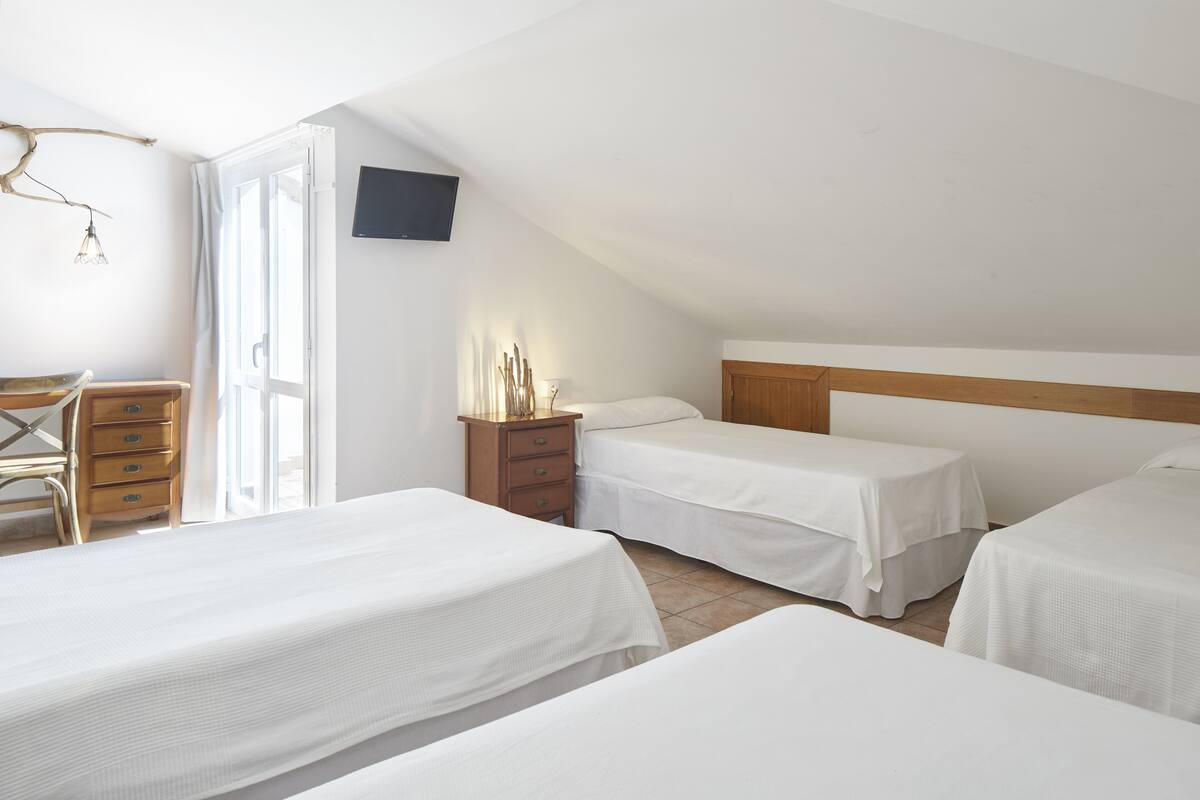 A bedroom with three beds, a desk, and a TV mounted on the wall.