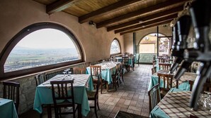 An indoor dining area with tables set for two, large arched windows offering a view of the countryside, and a rustic wooden ceiling. - Country House Le Vedute (Trevi)
