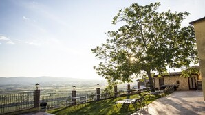 A patio with outdoor seating, a stone building, and a view of the countryside. - Country House Le Vedute (Trevi)