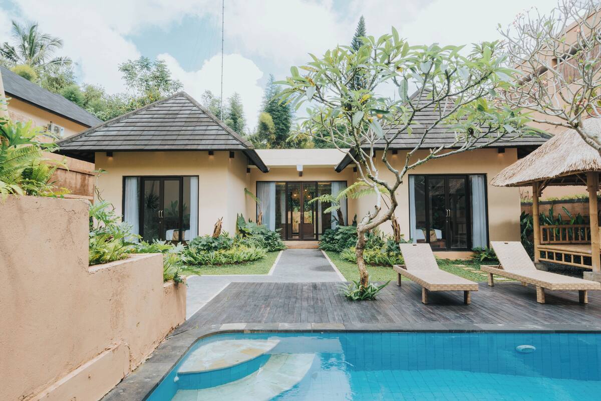 Una villa moderna con piscina, terraza de madera y estructura de techo de paja.