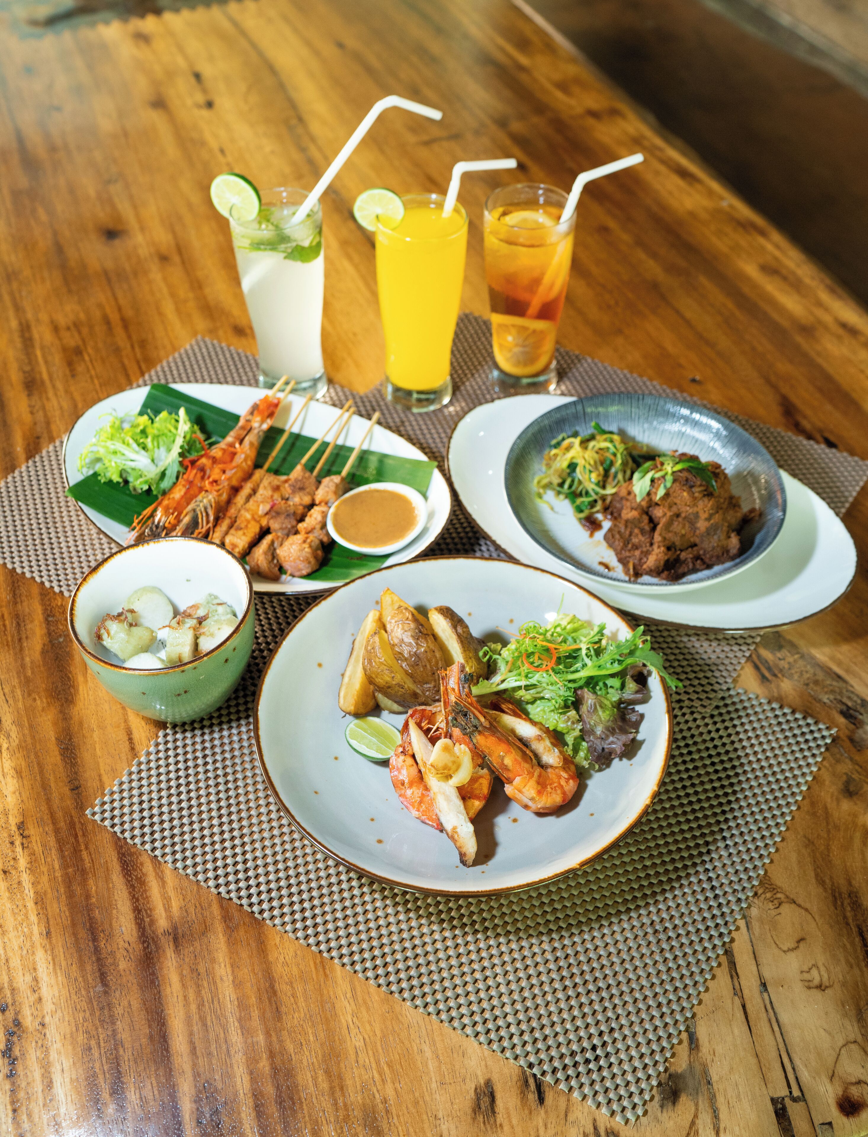 Une table en bois sur laquelle sont disposés divers plats, notamment des viandes grillées, des fruits de mer et des légumes, accompagnés de boissons.