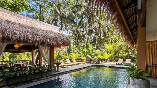 A pool area with lounge chairs, a thatched-roof structure, and lush tropical vegetation. - Alam Penari Ubud (Ubud)