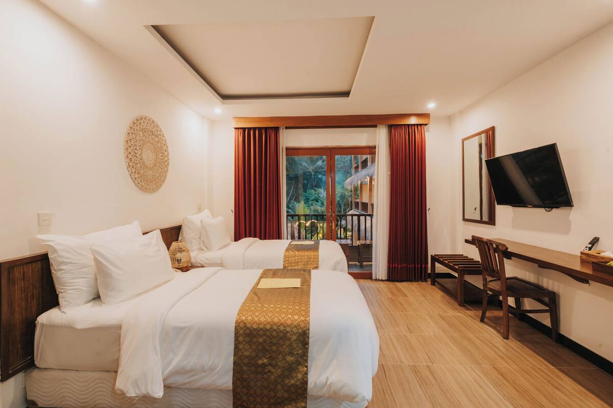 Habitación de hotel con dos camas, un escritorio, una silla, un televisor y un balcón con cortinas rojas.