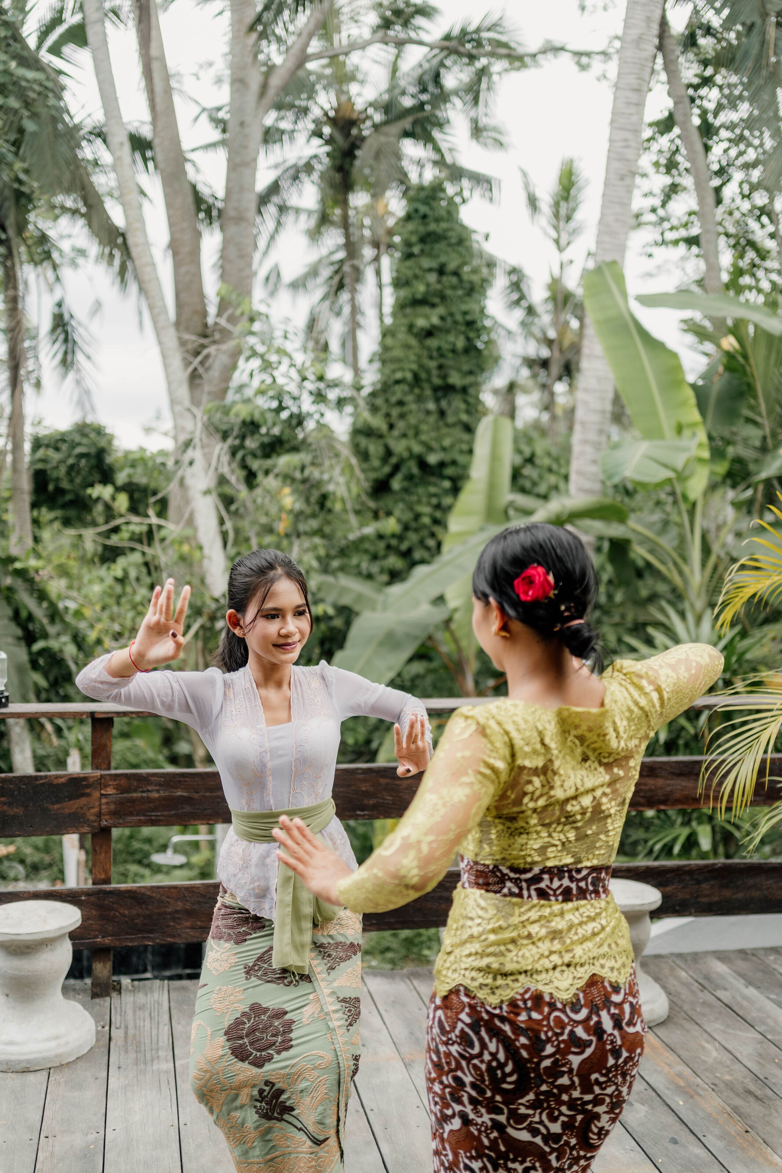Two people performing a traditional dance on a wooden deck with a tropical background.