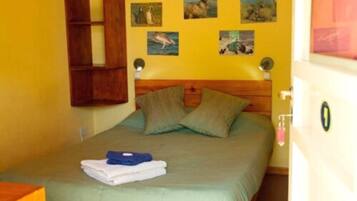 Cama de solteiro com cabeceira de madeira, colcha verde e duas almofadas. Quadros nas paredes retratam diversos animais.