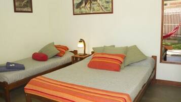 Quarto com duas camas de solteiro, cada uma com travesseiros e cobertor. Há uma mesa de cabeceira com luminária entre as camas.