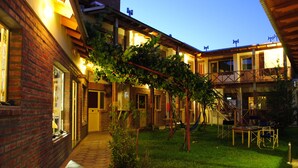 A brick building with a covered patio area, potted plants, and outdoor furniture. - La Tosca Hostel (Puerto Madryn)