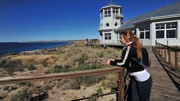 A coastal building with a lighthouse tower, a wooden deck, and a view of the ocean. - La Tosca Hostel (Puerto Madryn)