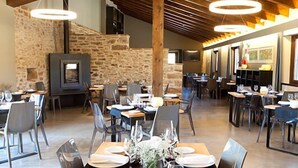 A restaurant with stone walls, wooden beams, and modern lighting. Tables are set with plates and glasses. - Hotel Mas de Cebrián (Puertomingalvo)