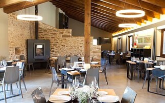 Un restaurante con paredes de piedra, vigas de madera e iluminación moderna. Las mesas están preparadas con platos y vasos.